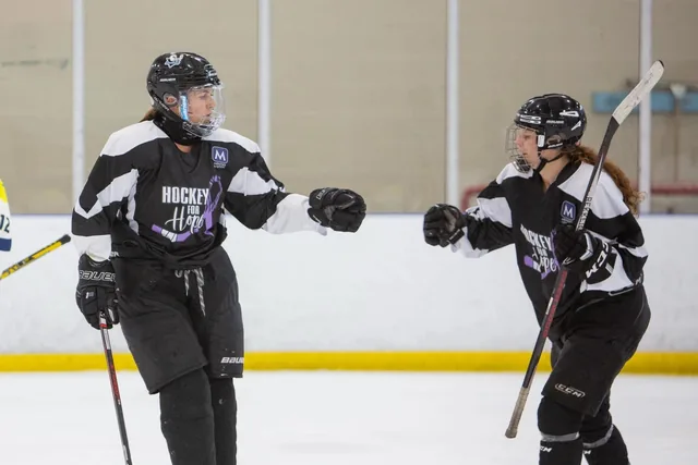 Two players in black and white Hockey for Hope jerseys bumping fists on the ice
