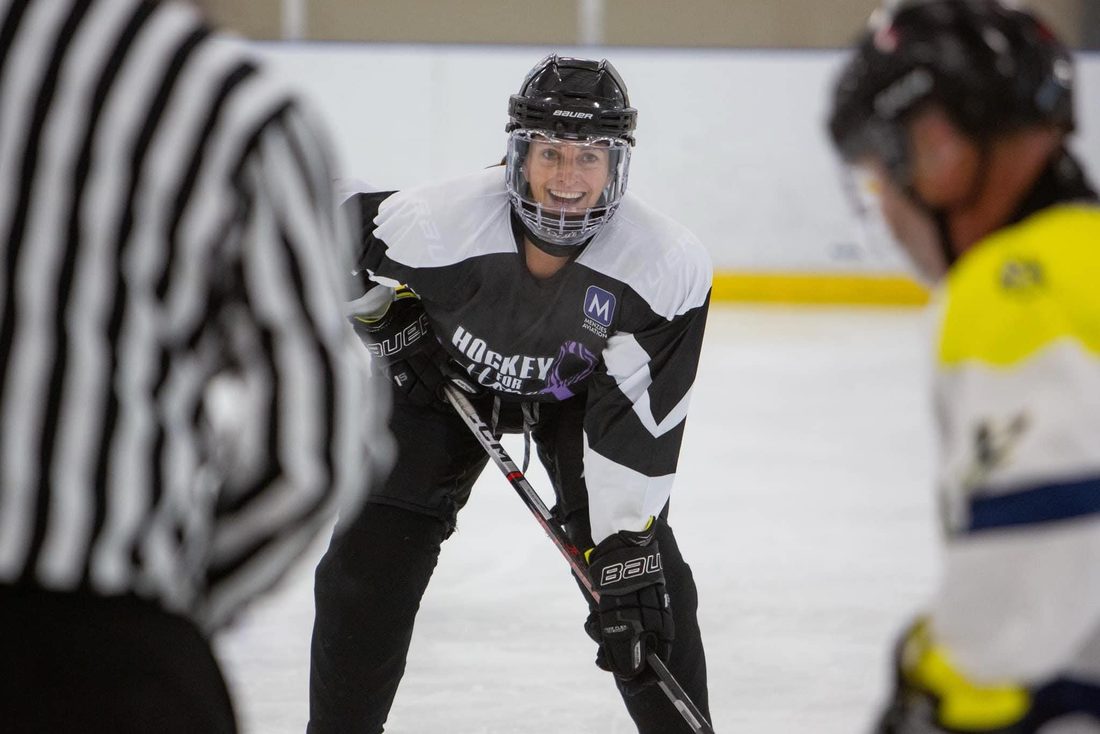 Shay Needham smiling in a black Hockey for Hope jersey as she lines up for a faceoff