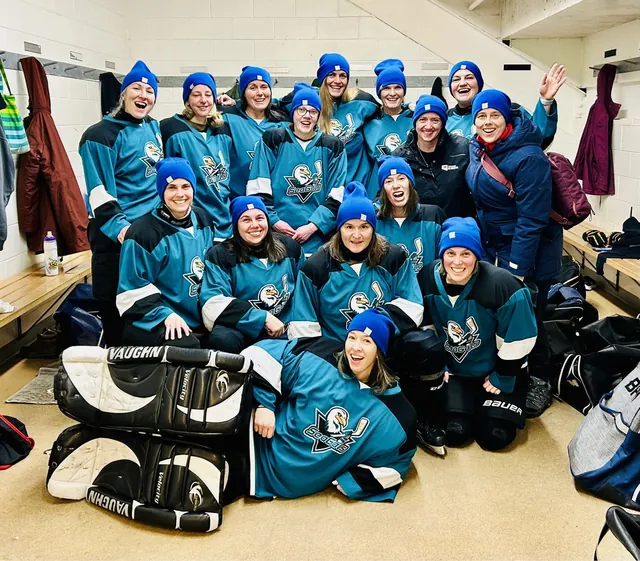A large team in teal jerseys and blue toques celebrating in the dressing room
