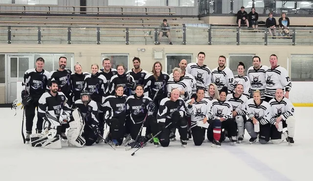 Two full rosters in black and white jerseys posing together on the ice after a game
